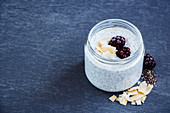 Tasty coconut chia seed pudding with blackberries in mason jar on grey stone background