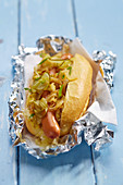 Hot dog with cucumber and onions in aluminium foil