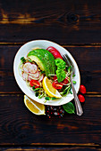 Top view of vegan quinoa salad with sprouts, tomatoes, avocado, radish and basil in bowl on dark rustic wooden background