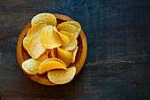 Crispy potato chips in bowl on wooden background