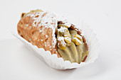 A sweet cannelloni filled with pistachio cream, in a paper case