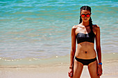 A young, dark-haired woman on a beach wearing a bikini