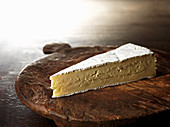 A piece of brie on a wooden plate