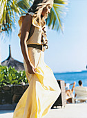 A young woman on a beach wearing a long, yellow dress