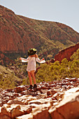 A young woman standing on rocks wearing a white blouse, shorts and a hat