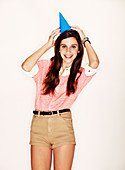 A young dark-haired woman with a party hat wearing a pink t-shirt and beige shorts