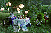 Gedeckter Tisch und farblich passender Stuhl unter beleuchteten Laternen im Garten