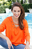 A brunette woman wearing an orange blouse with a lace tie