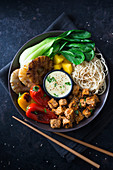 A vegan Buddha bowl with mie noodles, mango, pineapple, bok choy, grilled peppers, tofu and coconut curry sauce (Asia)