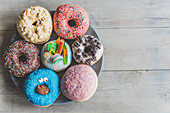 Verschiedenfarbige Krapfen und Donuts mit Zuckerstreuseln, Süssigkeiten und Nüssen