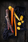 Rainbow carrots on a cloth against a wooden background (top view)