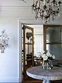 Glass vase with white roses on a round table, chandelier above