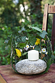 Candle on pebble surrounded by wreath of leaves as windbreak