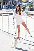 A girl wearing a white knitted jumper and shorts with a little dog