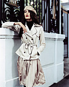 A dark-haired woman wearing a beret, a light trench coat and an matching skirt