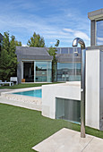 Water splashing from outdoor shower next to pool outside modern house