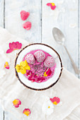 A frozen smoothie bowl with raspberries, pomegranate seeds and edible flowers