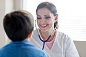 Nurse using stethoscope, smiling toward boy