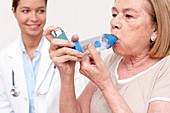 Senior woman using an inhaler, nurse watching