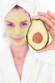 Woman holding avocado with face mask