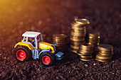 Toy tractor with stacked coins, conceptual image