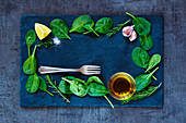 Top view of fresh delicious baby spinach leaves and olive oil on dark slate background