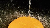 Water spraying on orange, slow motion