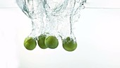 Four limes falling in water, slow motion