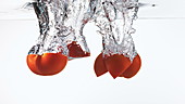 Cherry tomatoes falling in water, slow motion