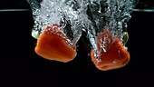 Red peppers falling in water, slow motion