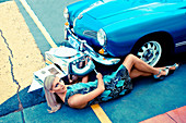 A blonde woman and a little boy dressed as a robot laying by a car