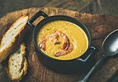 Corn creamy soup with shrimps served in individual pot with bread on board over rustic dinner table