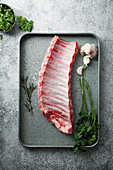 Uncooked pork ribs on metallic tray with herbs and garlic