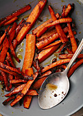 Close up shot of roasted caramelized carrots with olive oil and honey sauce in gray bowl