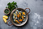 Shellfish Mussels Clams in copper cooking pan with parsley and lemon on concrete background