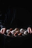 Variety of homemade dark chocolate truffles with cocoa powder, coconut, walnuts on vintage tray in kid's hands