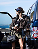 A young woman with a cup of coffee and a smartphone by a car