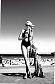 A blonde woman wearing a bathing suit with a drink on a beach (black-and-white shot)