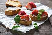 Toasted baguette slices with almond cream cheese, strawberries and basil (vegan)