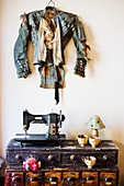 Designer-Jacke an der Wand, darunter Vintage Nähmaschine und Tassen aus Pappmache auf Kommode
