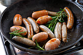 Various sausages with rosemary in a pan