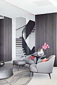 Dark gray designer armchairs and side table with flower vase in living room in front of stairs