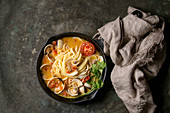 Pasta spaghetti Vongole in tomato cream sauce in cast-iron pan with textile over old metal texture background