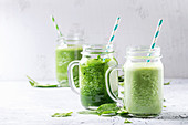 Variety of three color green spinach kale apple yogurt smoothie in mason jars with retro cocktail tubes over gray background
