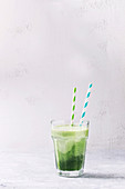 Glass of three color layer green spinach kale apple yogurt smoothie with retro cocktail tubes over gray background