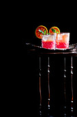 Blutorangen-Cocktails auf Tablett und Beistelltisch vor schwarzem Hintergrund