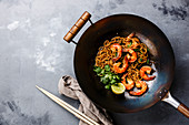 Ramen stir-fry noodles with shrimp in wok pan on gray concrete background copy space