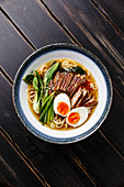 Ramen noodles with Duck, egg and pak choi cabbage in bowl on wooden background