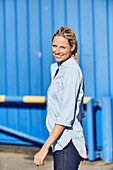 Blonde Frau in hellblauer Hemdbluse und Jeans vor blauer Hintergrund