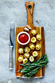 Wooden cutting board with homemade raw Italian tortellini, tomato sauce and rosemary over concrete textured background